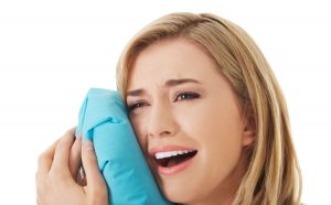 Woman experiencing tooth ache, holding ice bag - Emergency Toothache