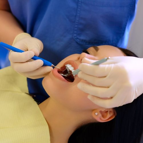Dentist hands working on young woman patient with dental tools.